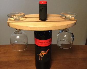 May include: Wooden wine bottle and glass holder with two wine glasses hanging from the sides. The bottle is labeled "Yellow Tail Cabernet Sauvignon".