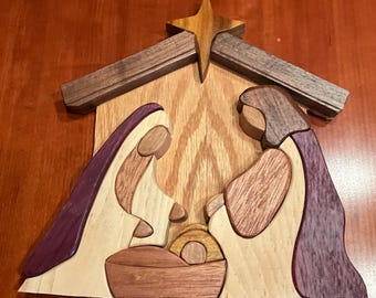 May include: Wooden nativity scene featuring Mary, Joseph, and baby Jesus in a manger. The figures are crafted from various wood tones, with purple and brown accents. A star sits atop the stable, adding a festive touch to this religious artwork.