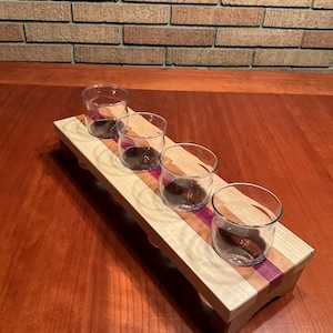Puede incluir: Una bandeja de servir de madera con cuatro vasos de vidrio transparentes. La bandeja está hecha de madera de arce y de corazón púrpura y tiene un acabado natural. La bandeja es perfecta para servir bebidas o aperitivos.