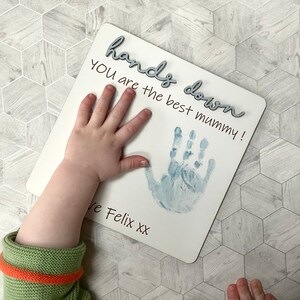 May include: White wooden sign with the text "hands down you are the best mummy!" and two blue handprints. The sign is signed "Love Felix xx".
