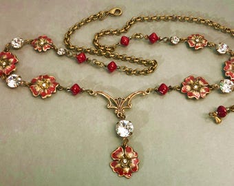 Könnte beinhalten: Eine goldene Kettenkette mit roten und klaren Perlen und roten und goldenen Blumenanhängern. Die Kette hat einen Anhänger mit einem großen klaren Kristall und einem kleineren roten und goldenen Blumenanhänger.
