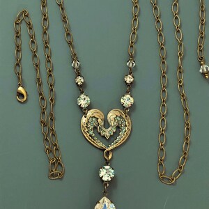 May include: A gold-toned necklace featuring a heart-shaped pendant adorned with crystals and a large teardrop crystal. The chain is a delicate link design. The necklace is approximately 45 cm in length, with a lobster clasp.
