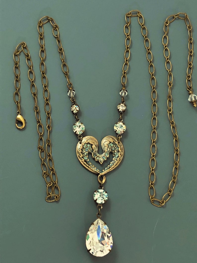 May include: A gold-toned necklace featuring a heart-shaped pendant adorned with crystals and a large teardrop crystal. The chain is a delicate link design. The necklace is approximately 45 cm in length, with a lobster clasp.
