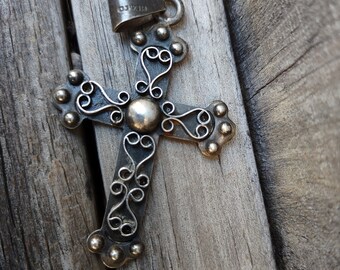 May include: A silver cross pendant with intricate filigree and beaded details. The cross features a central sphere and decorative swirls. The pendant is marked with "925" and "MEXICO".