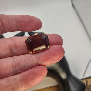 May include: A dark brown, rectangular, faceted glass stone with gold-toned metal trim.