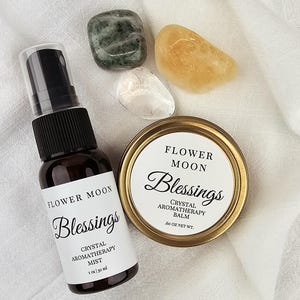 May include: A set of two crystal aromatherapy products from Flower Moon. The set includes a 1 ounce bottle of crystal aromatherapy mist and a 0.6 ounce jar of crystal aromatherapy balm. Both products feature the text "Blessings" and are packaged in a white label with black text.