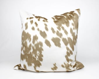 May include: A white and brown throw pillow with a cowhide pattern. The pillow is made of a soft, plush fabric and is perfect for adding a touch of rustic charm to any room.