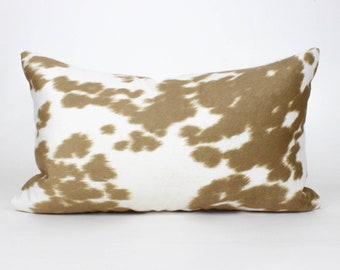 May include: A rectangular decorative pillow with a cowhide pattern. The pillow features a white background with irregular brown patches, creating a natural, rustic aesthetic. The pillow is designed for home decor.