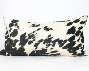 May include: A black and white cowhide patterned lumbar pillow. The pillow is rectangular and has a soft, plush feel.