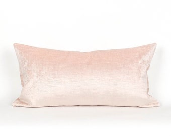 May include: A rectangular blush pink velvet pillow. The pillow has a soft, textured appearance and is designed for decorative use. The pillow is a light pink color and is set against a white background.