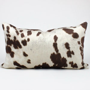 May include: A rectangular brown and white cowhide pillow with a brown and white spotted pattern.