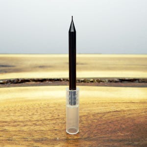 May include: A black, pointed, metal tool with a clear plastic handle. The tool is sitting on a wooden surface.