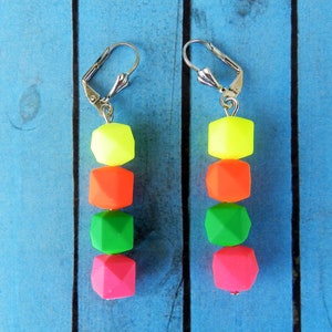 Puede incluir: Un par de pendientes de colores ne&oacute;n con un gancho plateado. Los pendientes est&aacute;n hechos de cuatro cuentas, cada una de un color diferente: amarillo, naranja, verde y rosa.