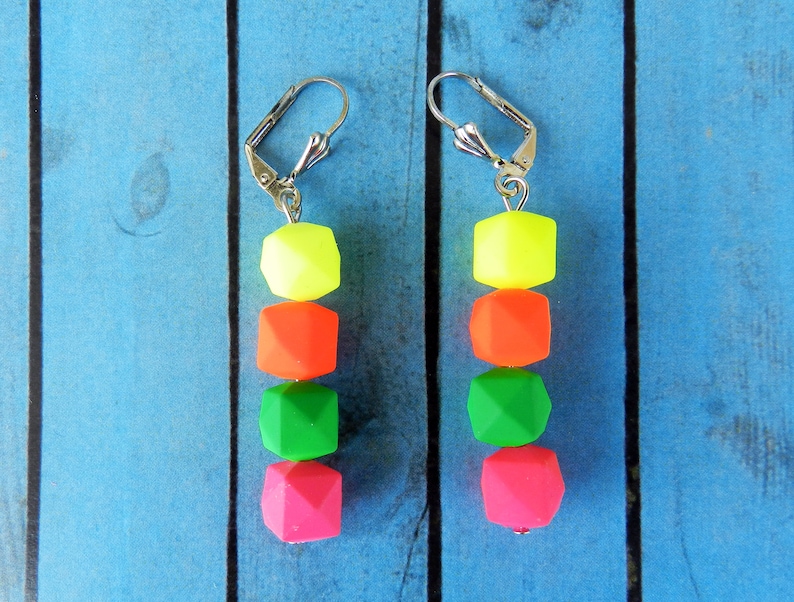 Puede incluir: Un par de pendientes de colores ne&oacute;n con un gancho plateado. Los pendientes est&aacute;n hechos de cuatro cuentas, cada una de un color diferente: amarillo, naranja, verde y rosa.