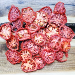 May include: A selection of dried tomato slices, displaying a rich red colour with visible seeds and textures. The tomatoes are arranged on a wooden surface, emphasising their natural form and preparation.