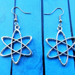 May include: A pair of silver atom earrings with a simple design. The earrings are hanging from silver hooks.