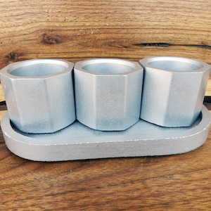 May include: Three silver hexagonal shot glasses with a matching silver tray. The glasses and tray are made of concrete.