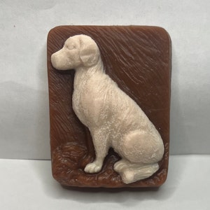 May include: A white dog soap bar with a brown background. The dog is sitting with its head turned to the side.