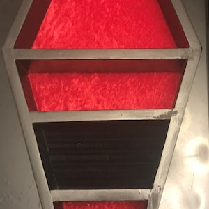 May include: A black wooden coffin-shaped jewellery box with red velvet lining and a black velvet bottom shelf. The box has three shelves and a top compartment with five small holes for earrings.