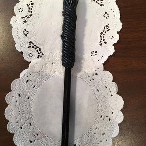 May include: A black wand with a green orb at the top. The wand is decorated with a black, rope-like design.