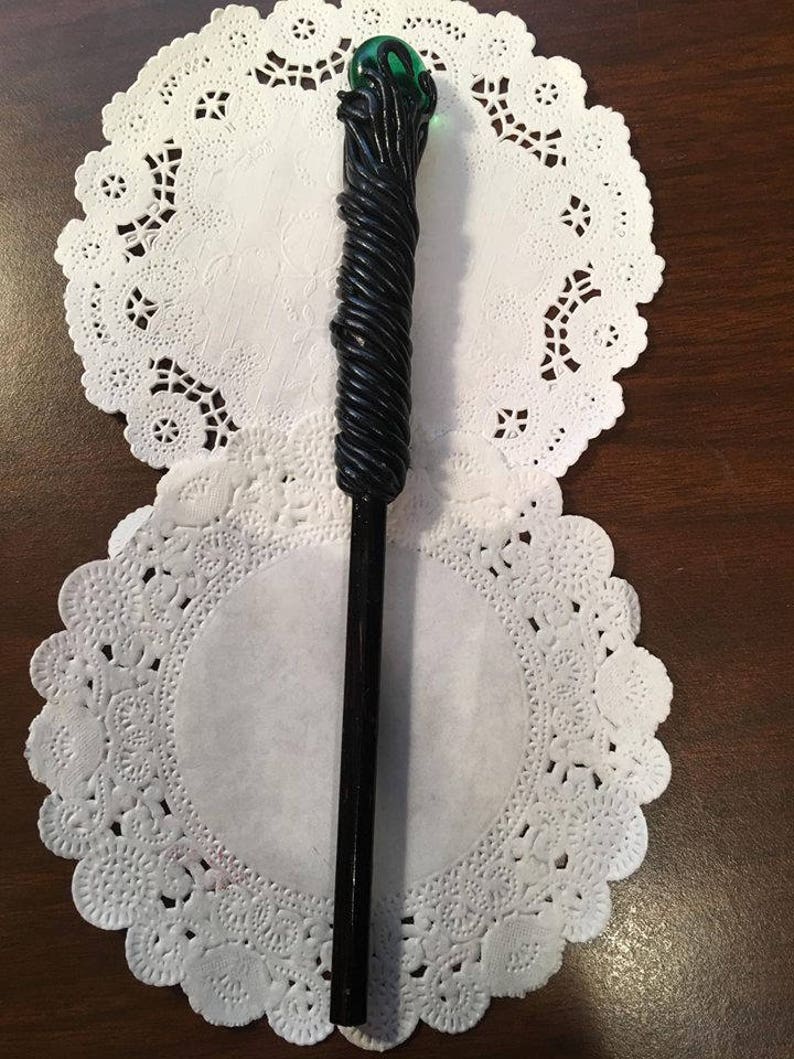 May include: A black wand with a green orb at the top. The wand is decorated with a black, rope-like design.