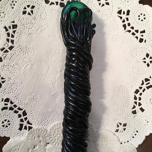 May include: A black and green wand with a green orb at the top. The wand is made of a twisted, rope-like material.