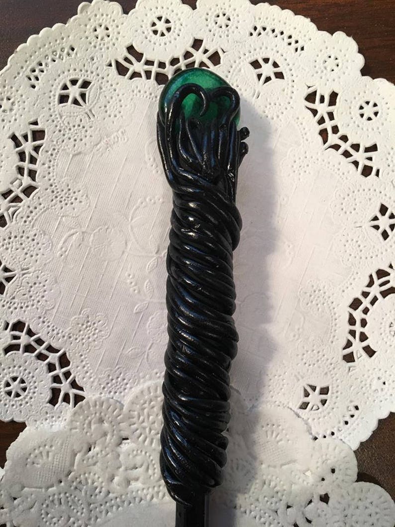 May include: A black and green wand with a green orb at the top. The wand is made of a twisted, rope-like material.
