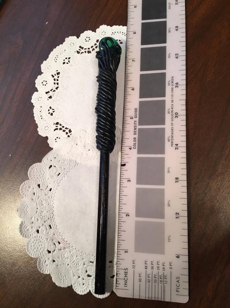 May include: A black and green wand with a twisted design and a green glass orb at the top. The wand is about 7 inches long and is measured against a ruler.
