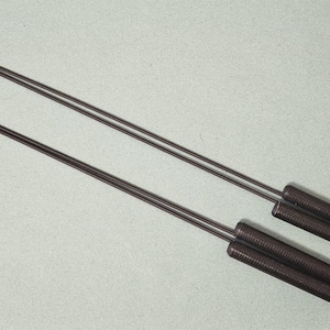 May include: Two dark gray metal roasting sticks with triangular tips and textured handles. The sticks are designed for grilling or roasting food over an open flame. The handles are approximately 3 inches long.