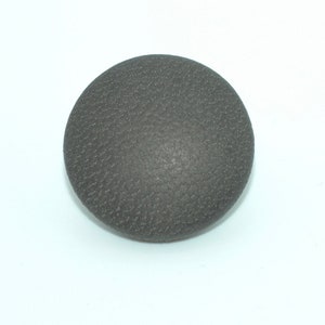 May include: A dark gray round button with a textured surface.