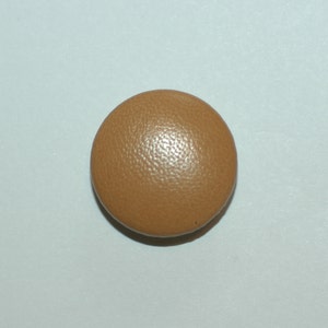 May include: A round, brown leather button with a textured surface.
