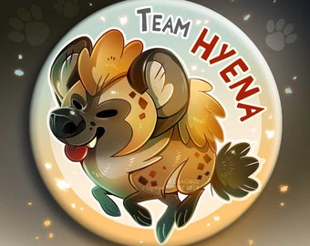 May include: A round button with a cartoon hyena in the center. The hyena is brown and yellow with black spots. The button has a light blue background with the text "TEAM HYENA" in white. The button also has the text "NEW BUTTON & MAGNET" in black. The button is surrounded by a gold border.