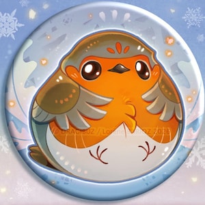 Peut inclure: Un bouton ou aimant rond avec une illustration de rouge-gorge de dessin animé. Le rouge-gorge a un plumage orange, gris et blanc. Le texte "NEW BUTTON & MAGNET" est affiché en dessous. Le fond est bleu clair avec des flocons de neige.
