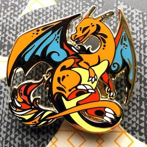 Può includere: Spilla in smalto arancione, giallo e blu di un drago con coda e ali arrotolate. Il drago ha un design dettagliato con contorni neri.