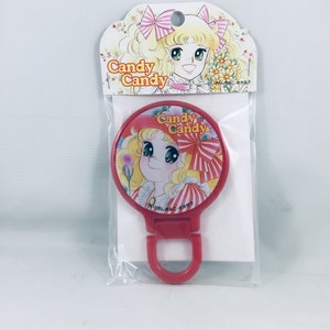 May include: A red Candy Candy compact mirror with a matching handle. The mirror features a cartoon illustration of a blonde girl with a red hat and a floral background. The packaging includes the Candy Candy logo and a floral design.