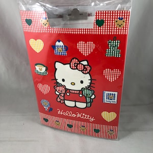 May include: Red Hello Kitty clipboard with a clear plastic top. The clipboard features a Hello Kitty graphic, hearts, and teddy bear designs. The background has a red and white checkered pattern. The words "Hello Kitty" are printed on the clipboard.