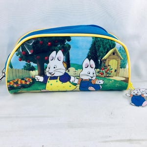 以下が含まれることがあります： 2匹の白いウサギの漫画イラストが描かれた、青と黄色のジッパー付きペンケース。ケースは青い上部、黄色のトリム、シルバーの留め金が付いています。お揃いのチャームが付いています。