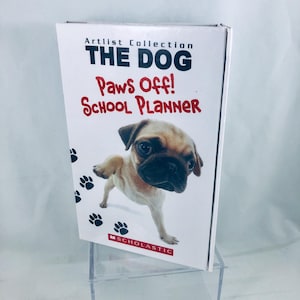 May include: A white school planner titled "THE DOG Paws Off! School Planner" from the Artlist Collection, featuring a pug puppy image. Black paw prints are scattered around the puppy. The Scholastic logo is at the bottom.