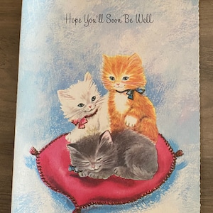 Puede incluir: Una tarjeta vintage de pronta recuperaci&oacute;n con tres gatitos en un coj&iacute;n rojo. La tarjeta tiene un fondo azul y el texto "Hope You'll Soon Be Well".