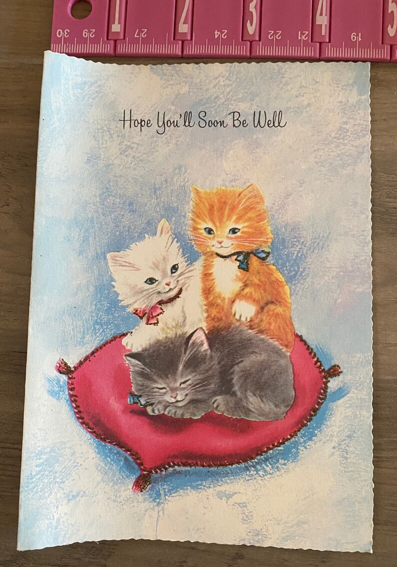 Puede incluir: Una tarjeta vintage de pronta recuperaci&oacute;n con tres gatitos en un coj&iacute;n rojo. La tarjeta tiene un fondo azul y el texto "Hope You'll Soon Be Well".