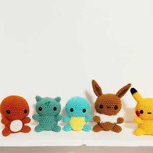 May include: Five crocheted Pokemon characters: a brown Charmander, a green Bulbasaur, a blue Squirtle, a brown Eevee, and a yellow Pikachu.