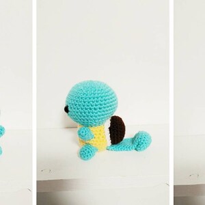 K&ouml;nnte beinhalten: Ein geh&auml;keltes Squirtle Pl&uuml;schtier in Blau, Gelb und Braun. Das Spielzeug sitzt auf einer wei&szlig;en Oberfl&auml;che.