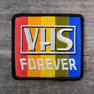 May include: A black and white embroidered patch with a rainbow stripe background. The patch says "VHS FOREVER" in white lettering.