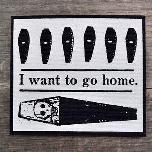 May include: Black and white patch with a row of five coffins and the text "I want to go home."