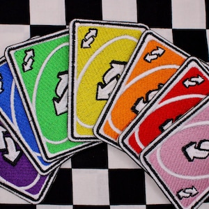 May include: A collection of colorful Uno reverse card patches. Each patch features a different color: purple, blue, green, yellow, orange, red, and pink. The patches are arranged on a black and white checkered background.