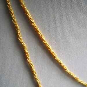 May include: Two strands of gold chain necklace, twisted together, on a white background.