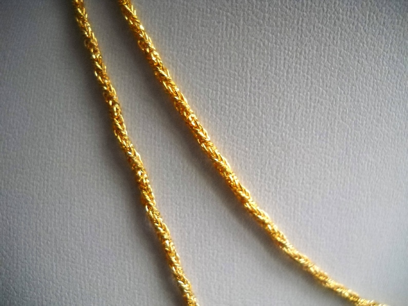 May include: Two strands of gold chain necklace, twisted together, on a white background.