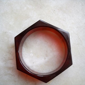 Pode incluir: Um bracelete hexagonal vermelho escuro feito de plástico.