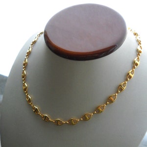 May include: A gold-colored chain necklace with a mariner link design. The chain is on a white display stand.