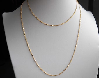 May include: A gold chain necklace with a delicate, linked design. The chain is layered, with one chain slightly longer than the other.